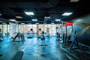 A gym with various exercise equipment, a wall with a geometric design, and a door leading outside. - Tulip Residences Muscat The Village (Seeb)
