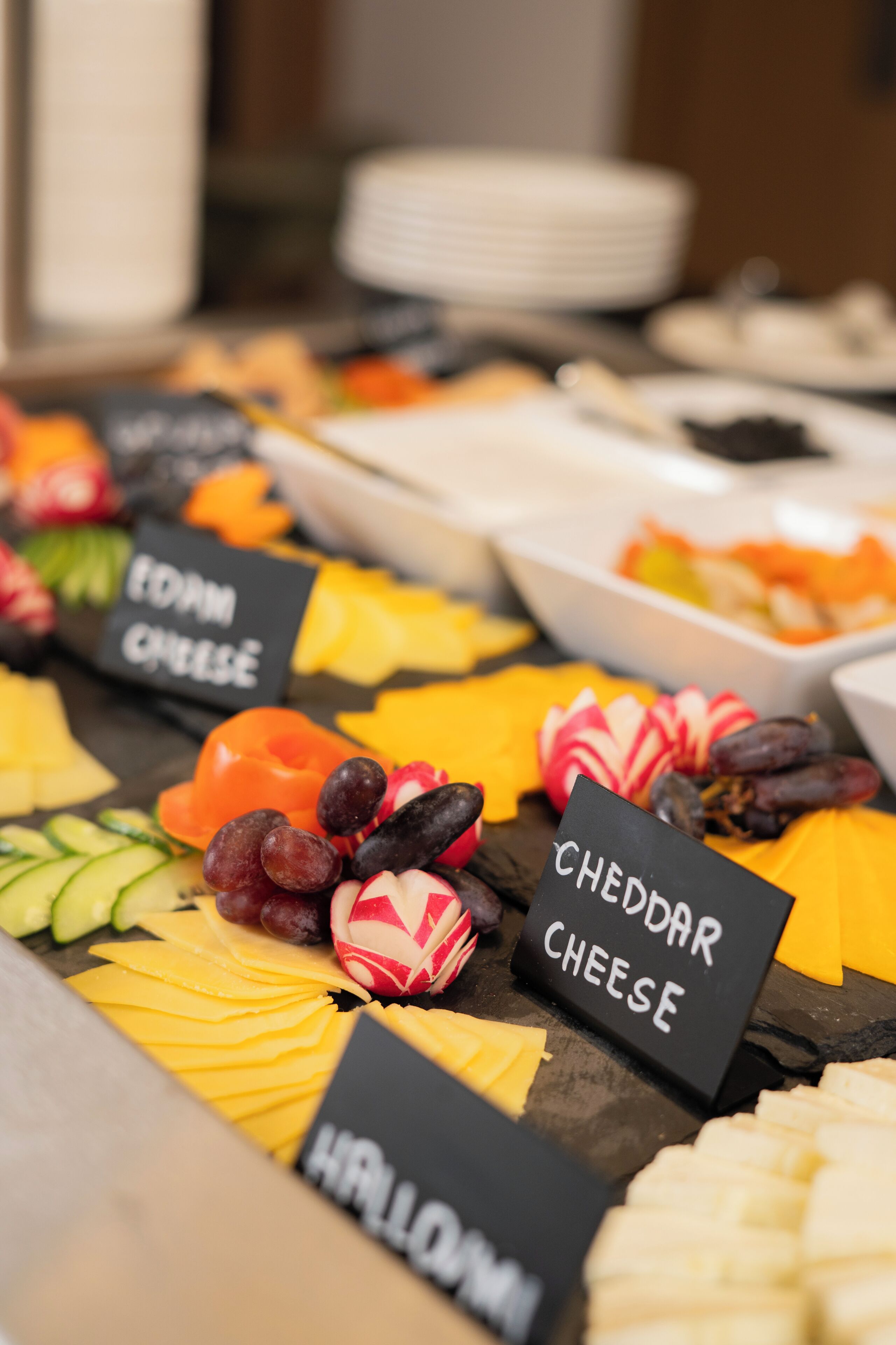 Una tabla de quesos y frutas con etiquetas para queso cheddar y jamón.