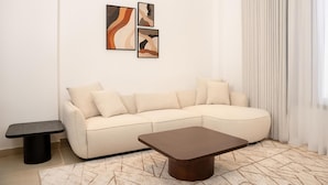 A living room with a beige sectional sofa, a dark wooden coffee table, and abstract art on the wall.