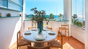 A round dining table with chairs, a vase with flowers, and a view of the ocean through large windows. - Beachfront Apartment in Puerto Banus Playa Rocio (Marbella)