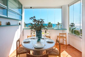 Ein runder Esstisch mit Stühlen, eine Vase mit Blumen und Meerblick durch große Fenster.