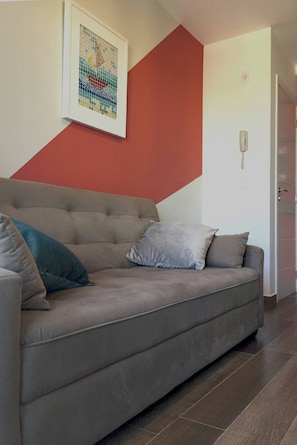 Un salón moderno con un sofá gris, una obra de arte enmarcada y una pared de acento roja.