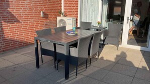 Eine Terrasse im Freien mit Tisch und Stühlen, einer Ziegelwand, einer Schiebetür aus Glas und einem Panasonic-Klimager ät.