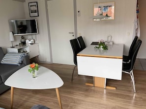 A modern living room with a sofa, a coffee table with flowers, a TV, a dining table with chairs, and a door. - 4 Star Holiday Home in Hemmet (Hemmet)