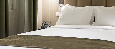 A hotel room with a bed, a bedside telephone, and a wall-mounted light fixture.
