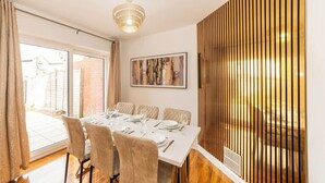 Un coin repas avec une table dressée pour six personnes, un lustre, une grande fenêtre et un mur recouvert de lambris en bois.