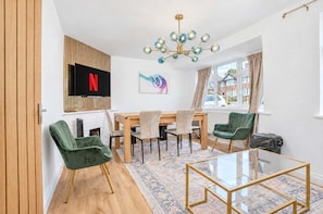 Ein modernes Wohnzimmer mit Fernseher, einem Esstisch und grünen Stühlen.