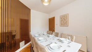 Un coin repas avec une longue table dressée pour quatre personnes, un paravent en bois et un radiateur fixé au mur.