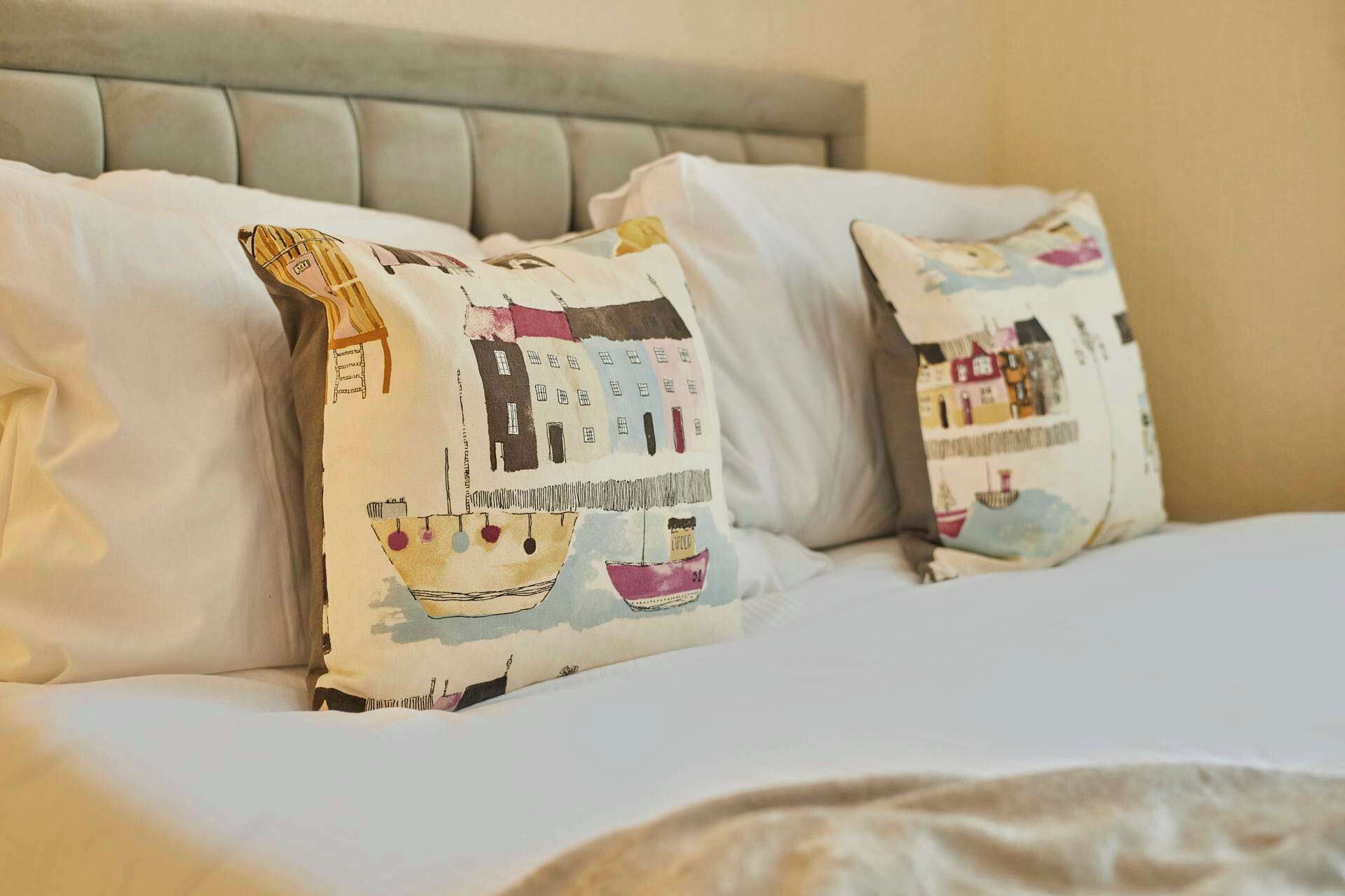 Ein Bett mit zwei Kissen, verziert mit bunten Illustrationen von Gebäuden und einem Boot.