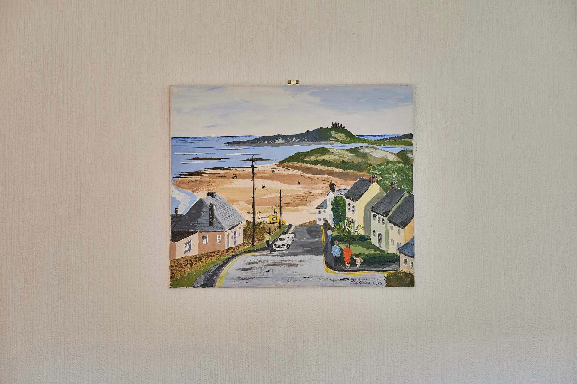 A coastal scene with buildings, a road, and a hill in the background.