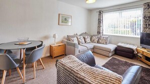 Ein Wohnzimmer mit einer Couch, einem Couchtisch, einem Fernseher und einem Fenster mit Vorhängen.