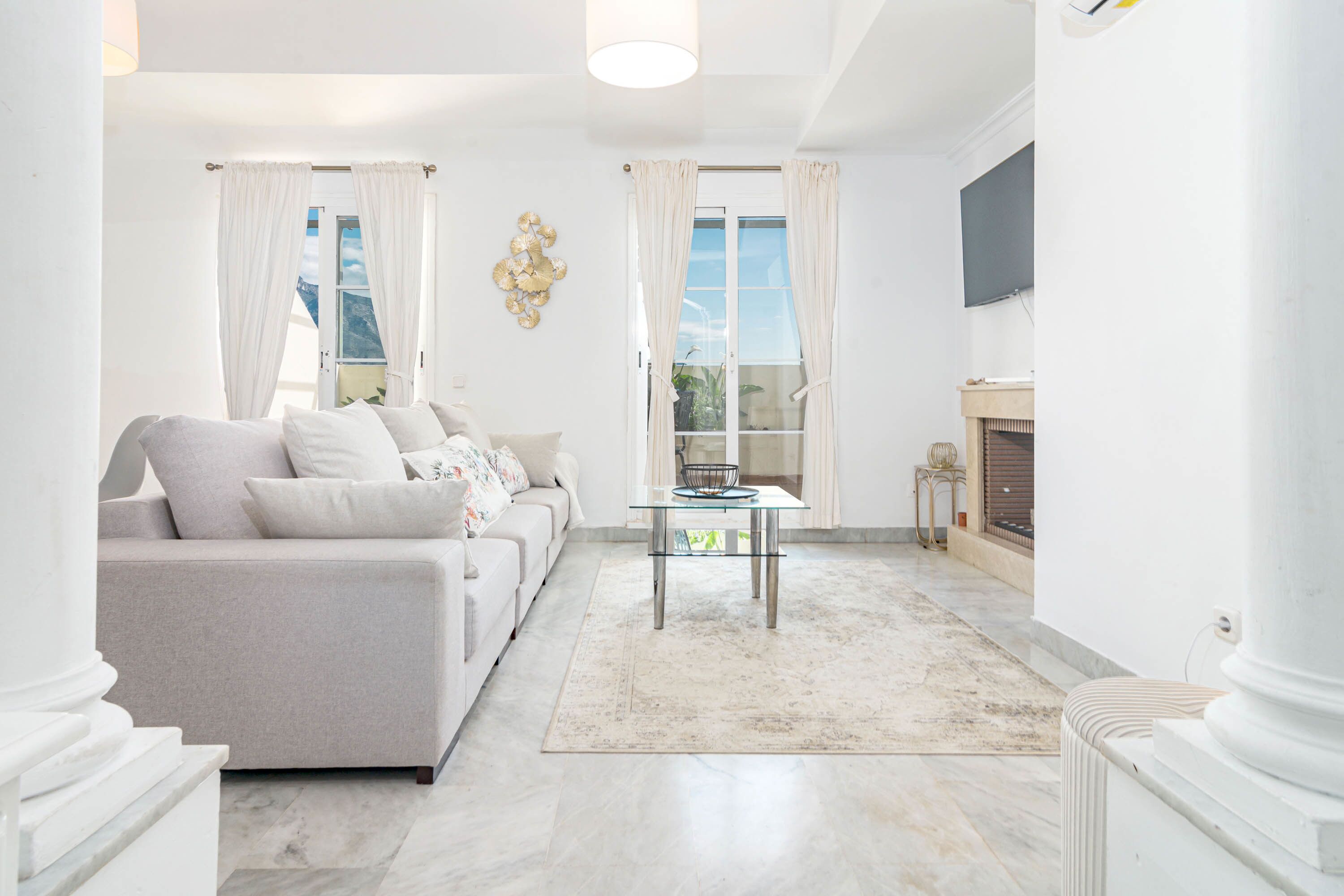A living room with a sofa, a glass coffee table, a fireplace, and a view through the windows.