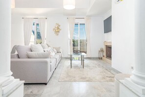 Ein Wohnzimmer mit einer Couch, einem Glastisch, einem Kamin und Blick durch die Fenster.