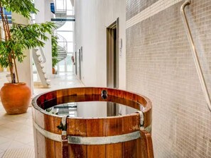 Eine Holztonne in einer Diele mit Fliesenwand, Blumentopf und Treppe im Hintergrund.