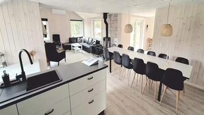 A modern kitchen with a central island, a dining area with a long table and chairs, and a view of the outdoors. - 4 Star Holiday Home in Romo (Rømø)