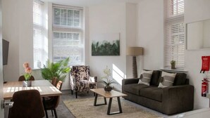 En moderne stue med spisebord, sofa, stole, pejs og et maleri på væggen.