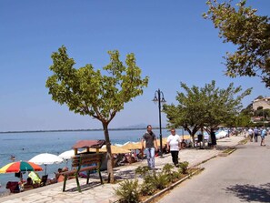 A coastal walkway with benches, umbrellas, and people.
