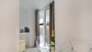 Une chambre moderne avec une table en verre, des chaises transparentes, une bouteille de champagne, une machine à café et un petit pouf.