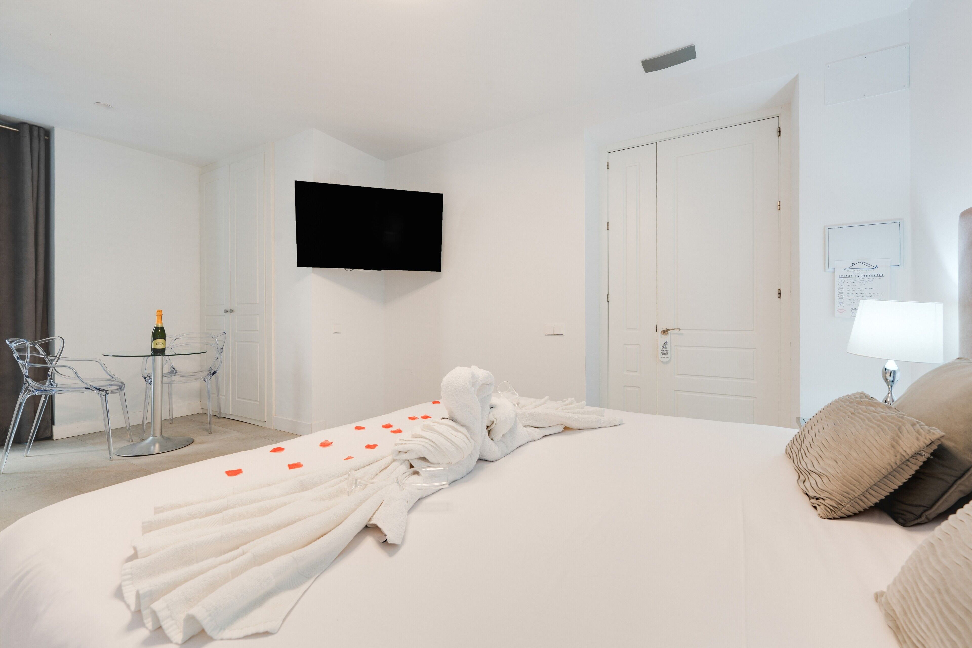 Hotelkamer met een bed, een aan de muur bevestigde televisie, een klein tafeltje met stoelen en een fles champagne.