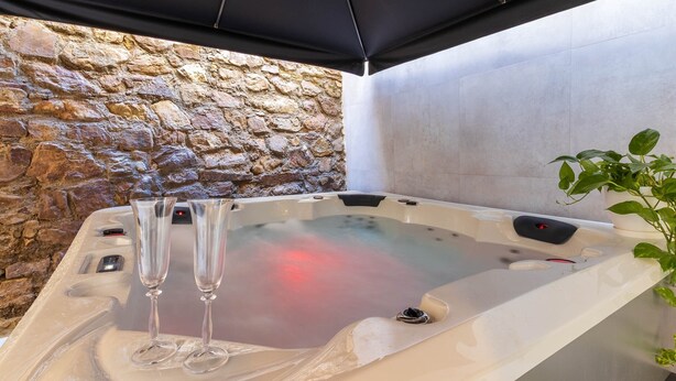 Un bain à remous avec deux verres, un mur en pierre et une plante en pot.