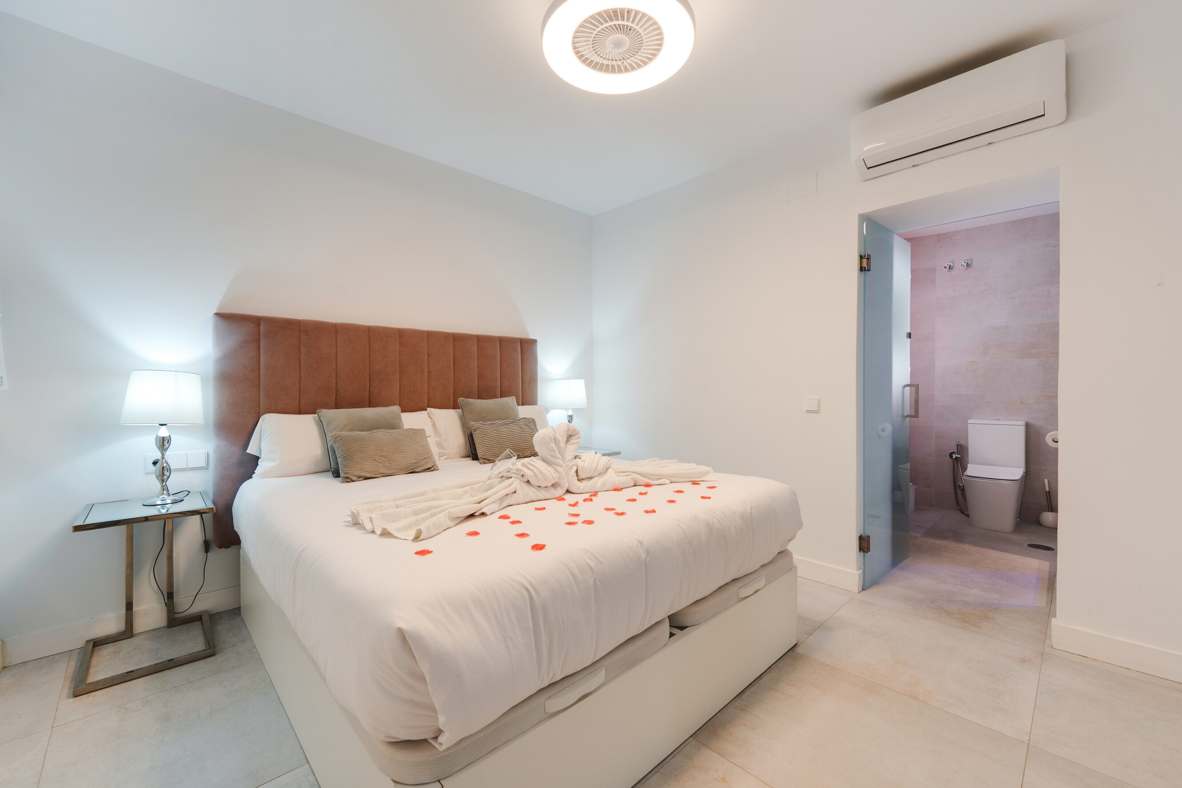 Une chambre d’hôtel avec un lit, des lampes de chevet, une table de chevet et une salle de bain visible à travers une porte ouverte.