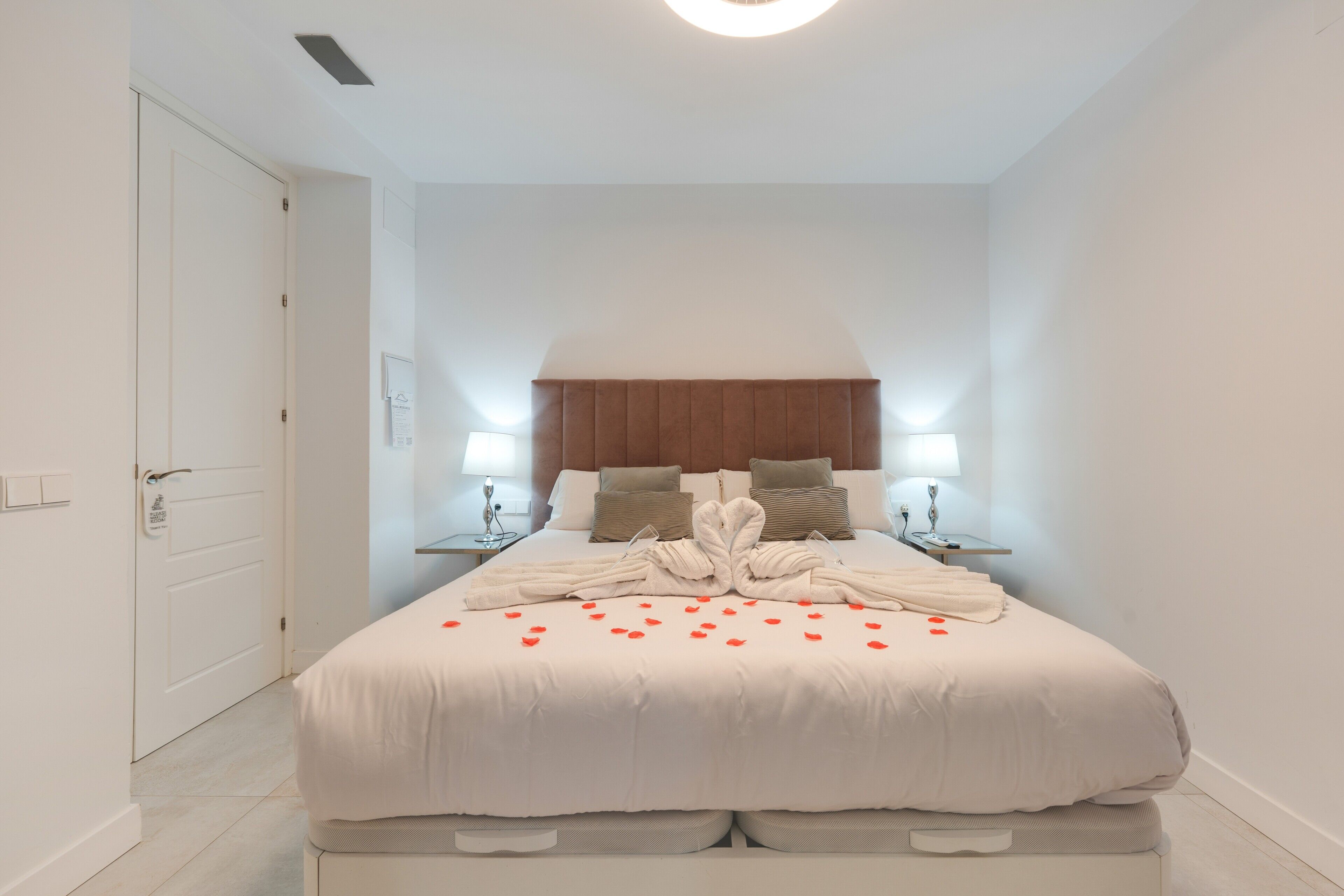 Una habitación de hotel con cama, dos mesitas de noche, una lámpara de techo y una puerta.