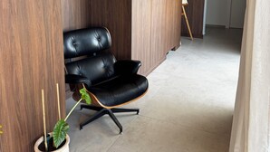 Una habitación moderna con una butaca de cuero negro, una planta en maceta, paneles de madera y piso blanco.