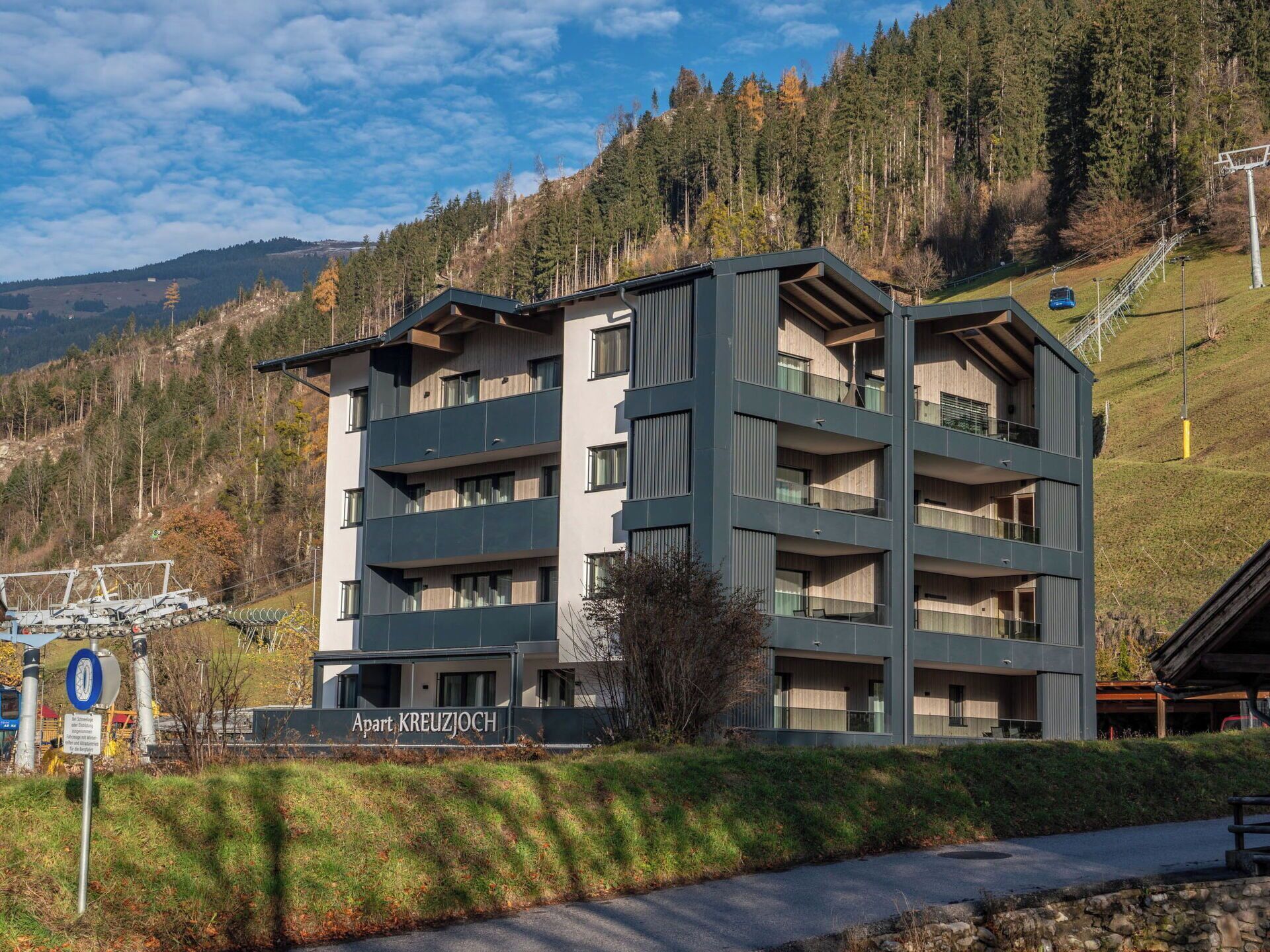 Ein mehrstöckiges Gebäude mit Balkonen, mit der Beschriftung 'Apart KREUZJOCH', vor einer Bergkulisse.