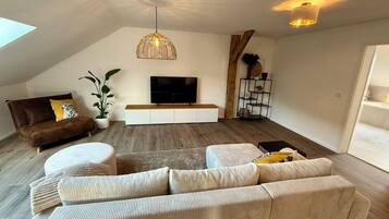 Una sala de estar moderna con techo inclinado, un televisor grande, un sofá marrón, un sofá beige y piso de madera.