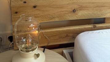 Cabecera de madera con una planta y un libro, una lámpara de cristal sobre una mesita de noche y una cama con ropa de cama blanca.