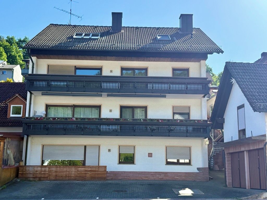 Ein zweistöckiges Wohnhaus mit Balkon, Garage und einem sichtbaren Schornstein.