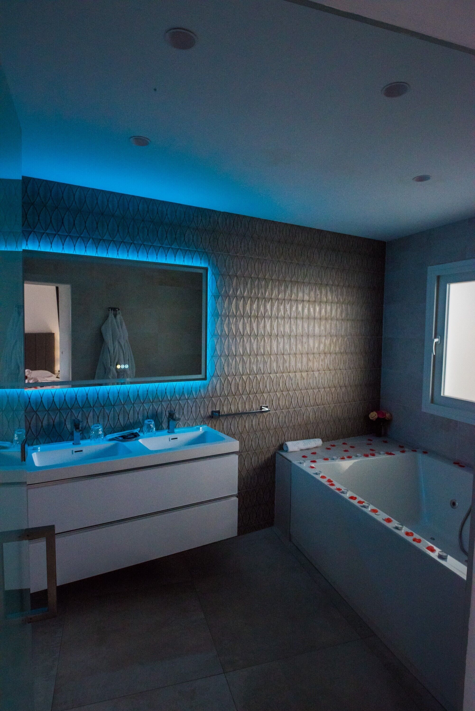 Een moderne badkamer met een grote spiegel, twee wastafels, een bad en een raam.