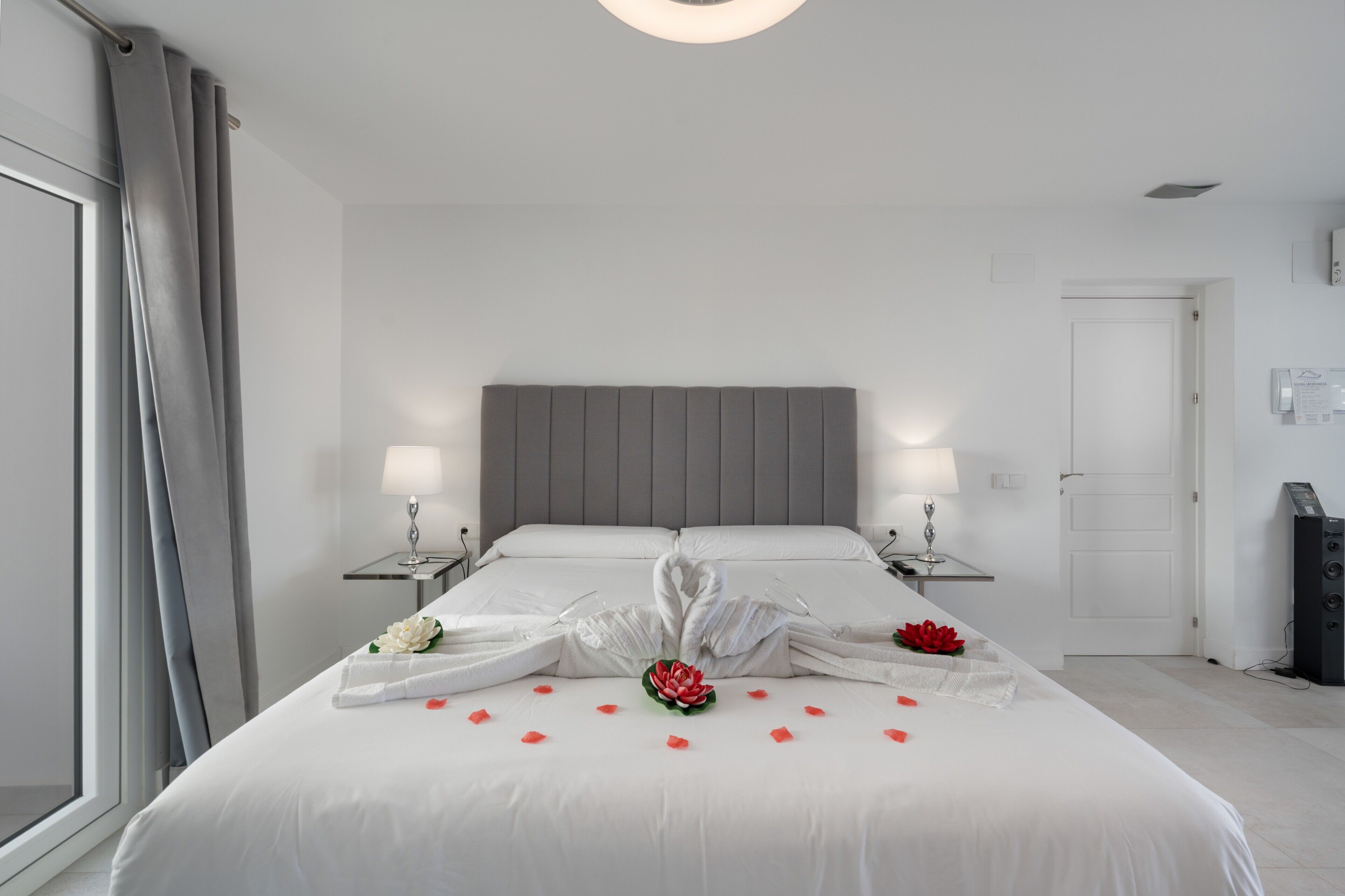 A hotel room with a large bed, two bedside tables with lamps, a grey headboard, and a white door.