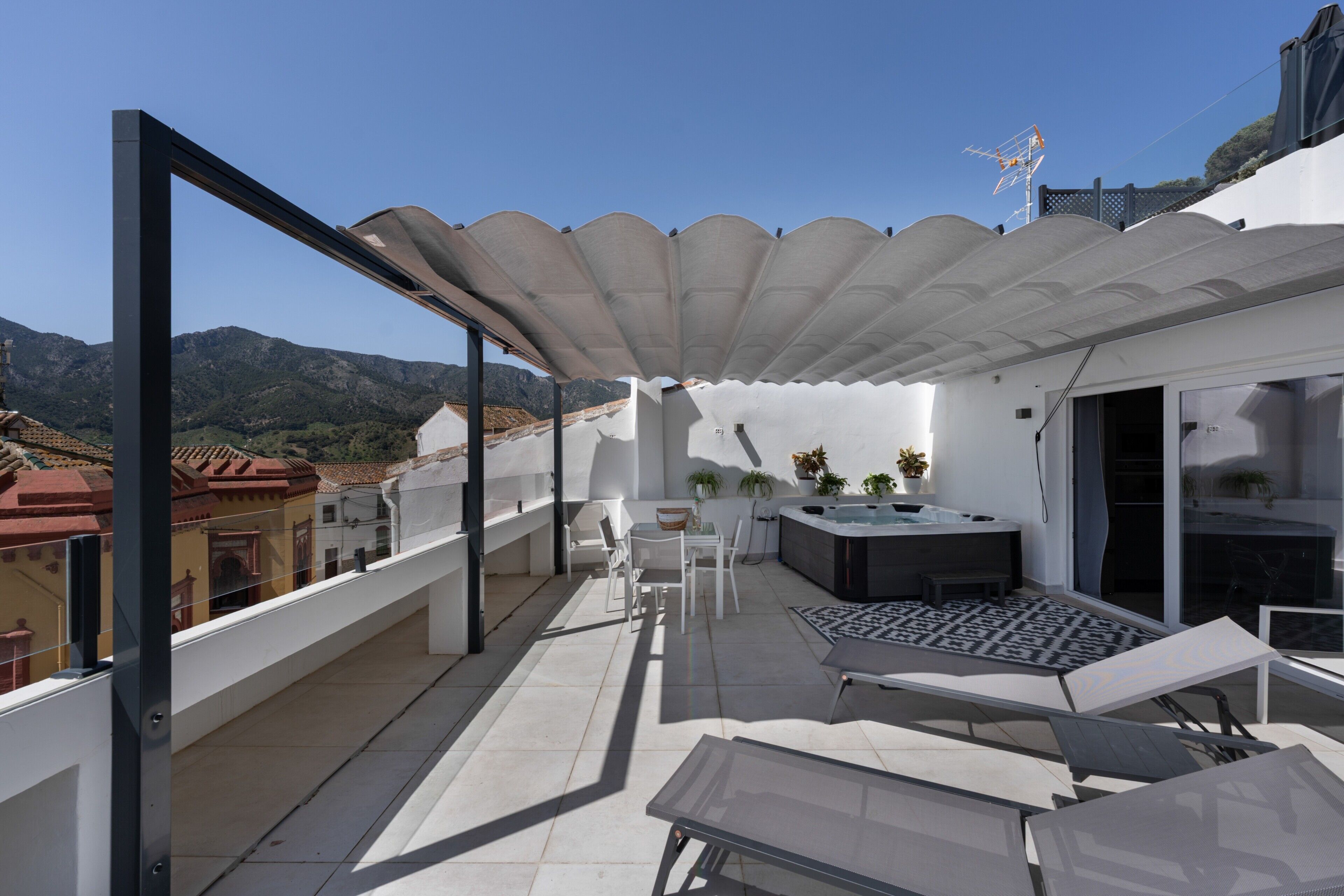 A rooftop terrace with a glass balustrade, a seating area with a table and chairs, and a hot tub.