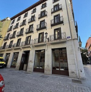 A multi-story building with a row of windows and balconies, a ground-floor entrance with a door, and a street in front. - Spacious & Bright 4-Bedroom Apartment in Central Madrid (Madrid)