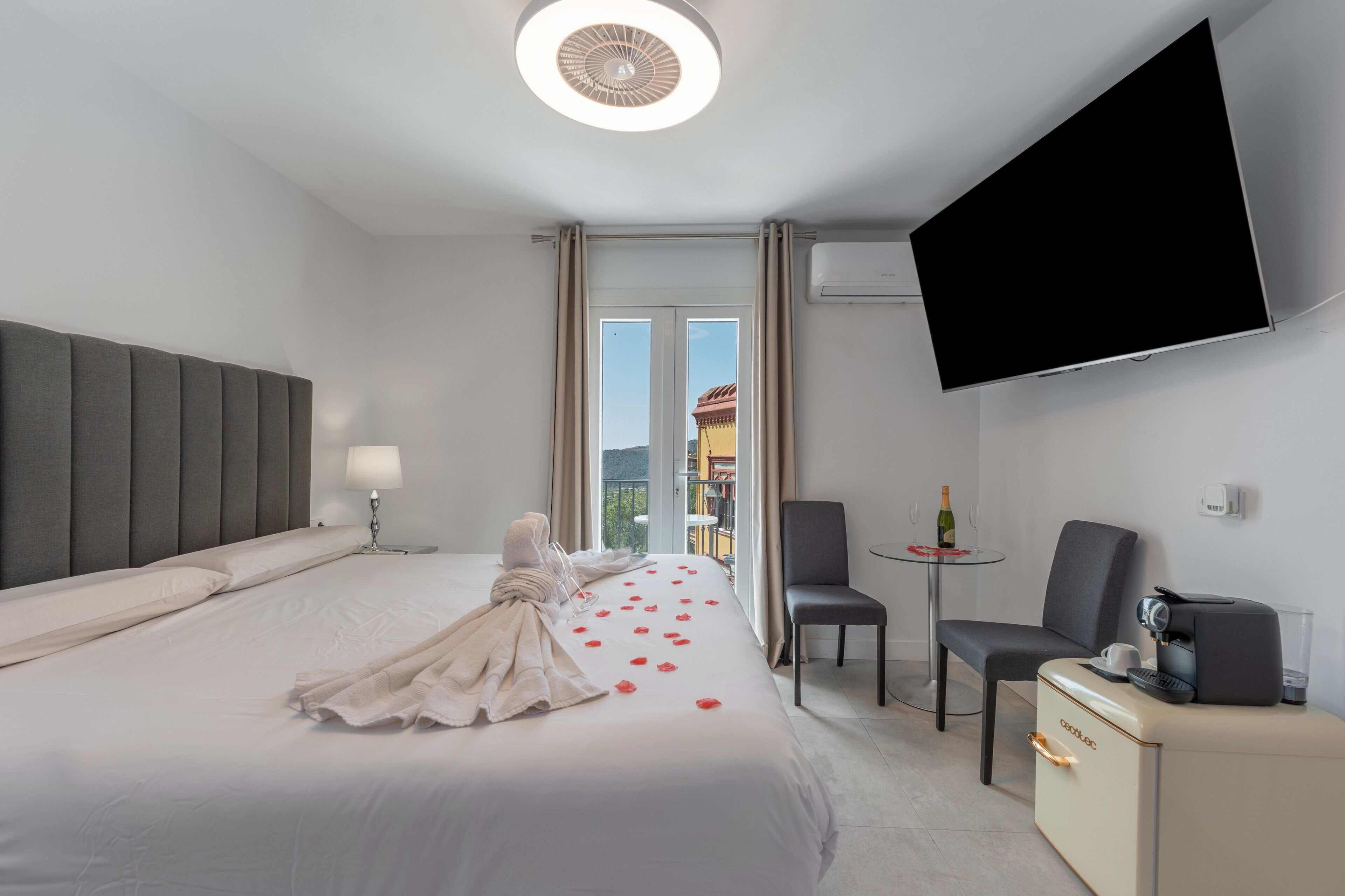 Ein Hotelzimmer mit Bett, Fernseher, Kaffeemaschine, Sessel und einem kleinen Tisch mit Flasche und Gläsern.