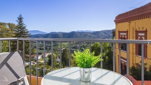 A balcony with a clear view of a mountainous landscape, a potted plant, and a yellow building with red trim. - Valeria Room: Double Whirlpool Bath, Mountain Views (Carratraca)