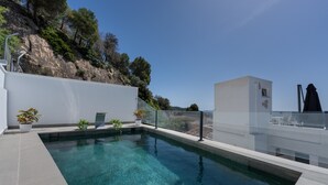 A modern outdoor swimming pool with clear water, surrounded by a white wall and potted plants. - Valeria Room: Double Whirlpool Bath, Mountain Views (Carratraca)