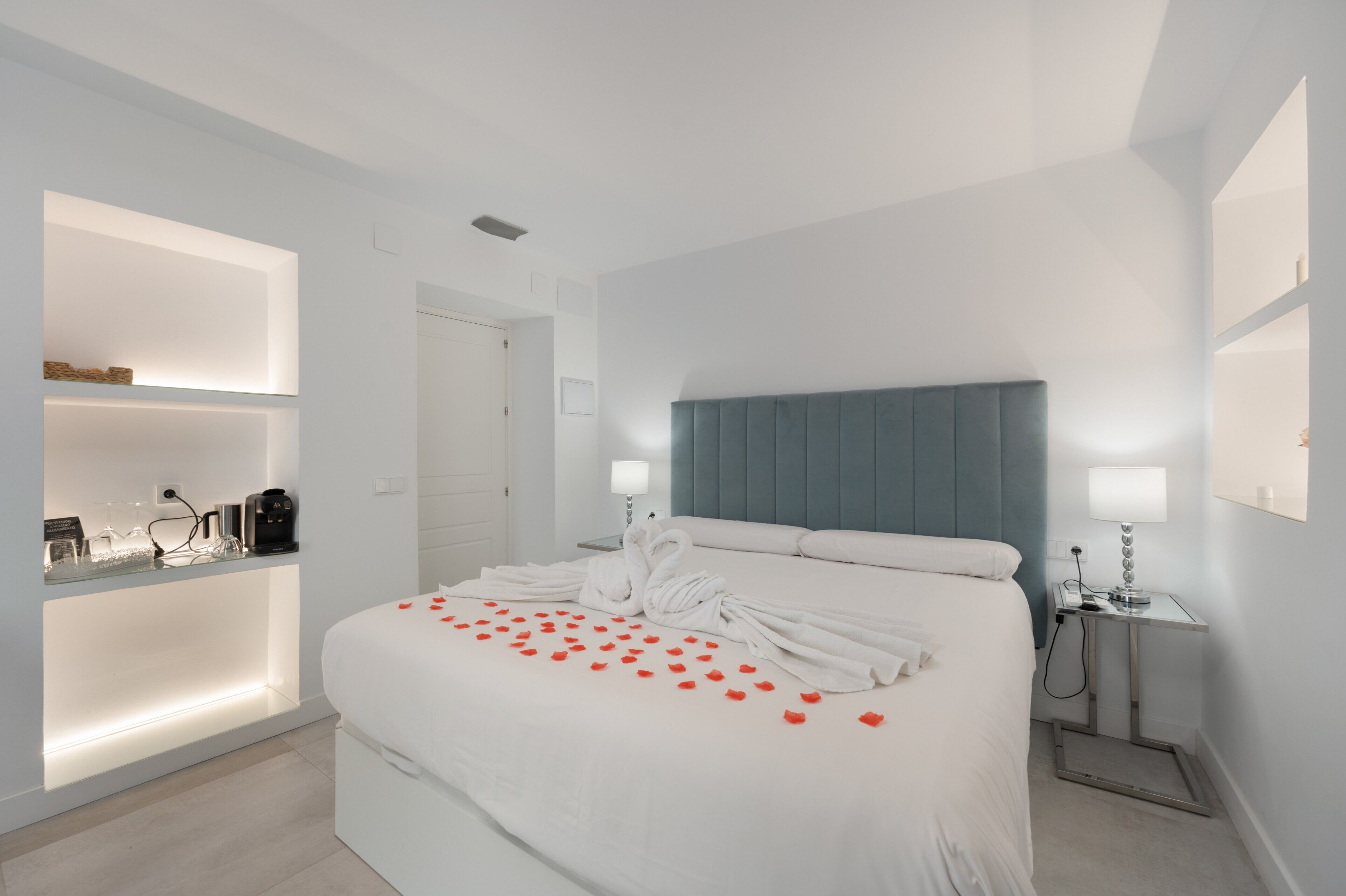 A hotel room with a bed, bedside tables, a nightstand, a built-in shelf, and a door.