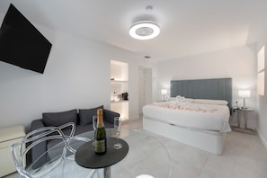 Ein modernes Hotelzimmer mit Bett, einer Sitzecke mit Tisch und einer Küchenzeile.