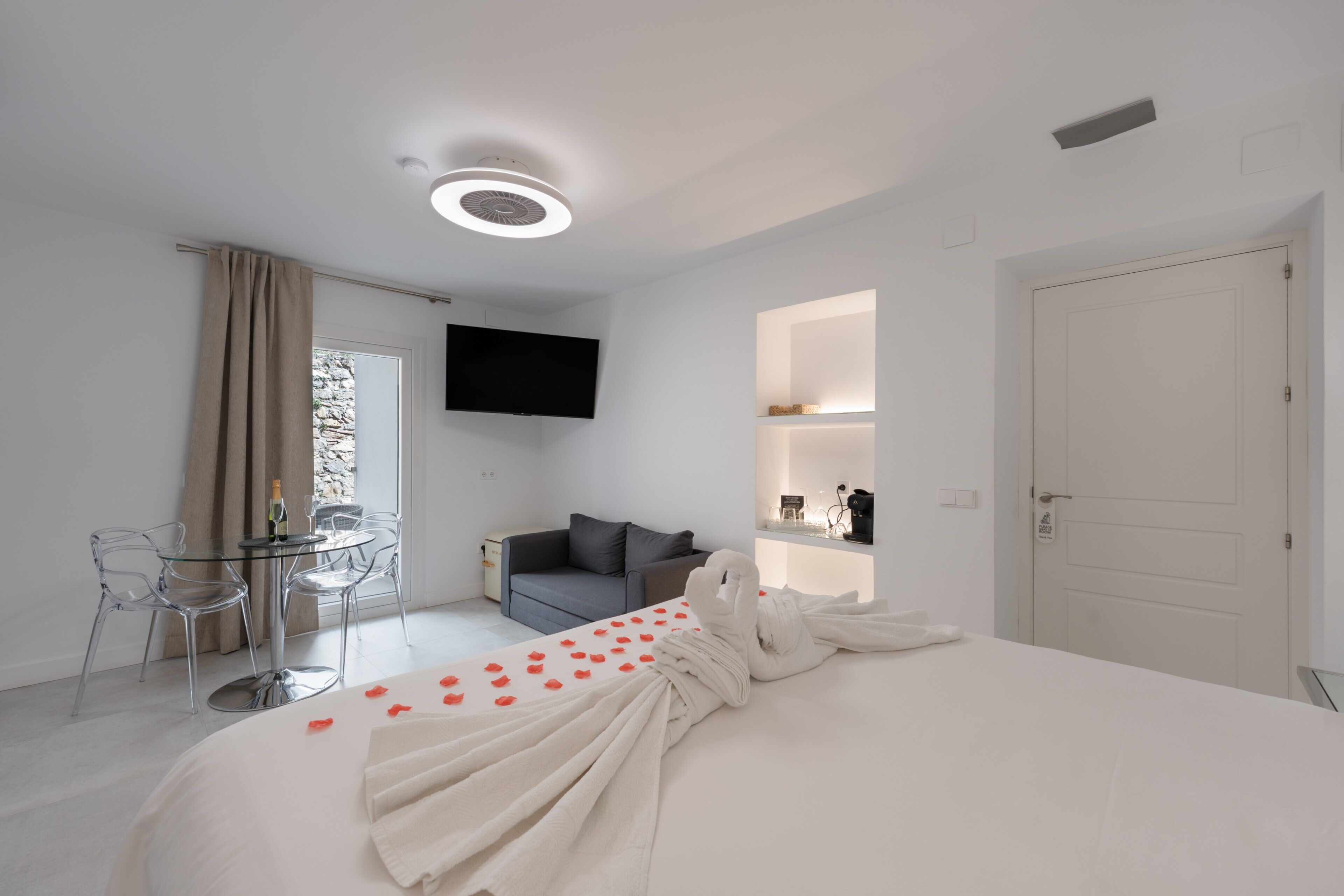 A hotel room with a bed, a TV, a sofa, a dining table, and chairs.