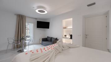 A hotel room with a bed, a TV, a sofa, a dining table, and chairs.