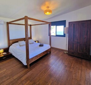 A four-poster bed with white linens, a bedside lamp, and a nightstand.