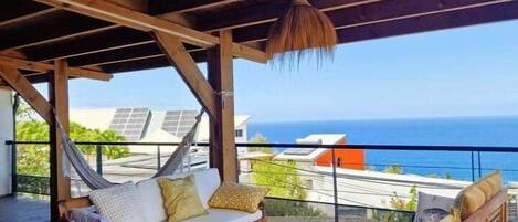 A wooden deck with a hammock, a round table, and a sofa with cushions.