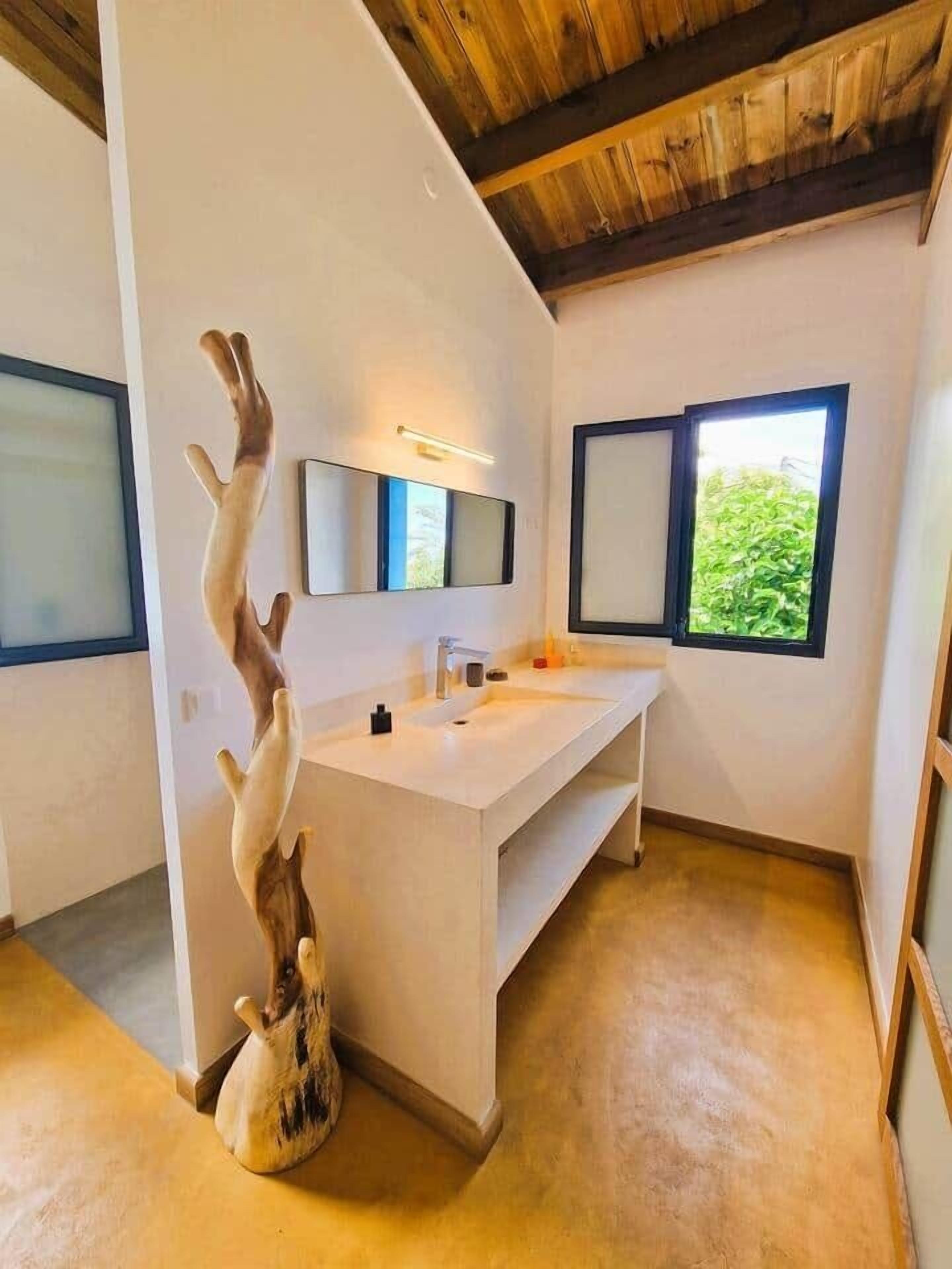 A bathroom with a white vanity, a mirror, and a wooden sculpture.