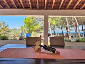 Ein überdachter Außenbereich mit Tisch, Stühlen und Blick auf das Meer.