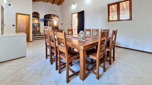 Un comedor con mesa y sillas de madera, una cocina al fondo y un techo alto con vigas a la vista.