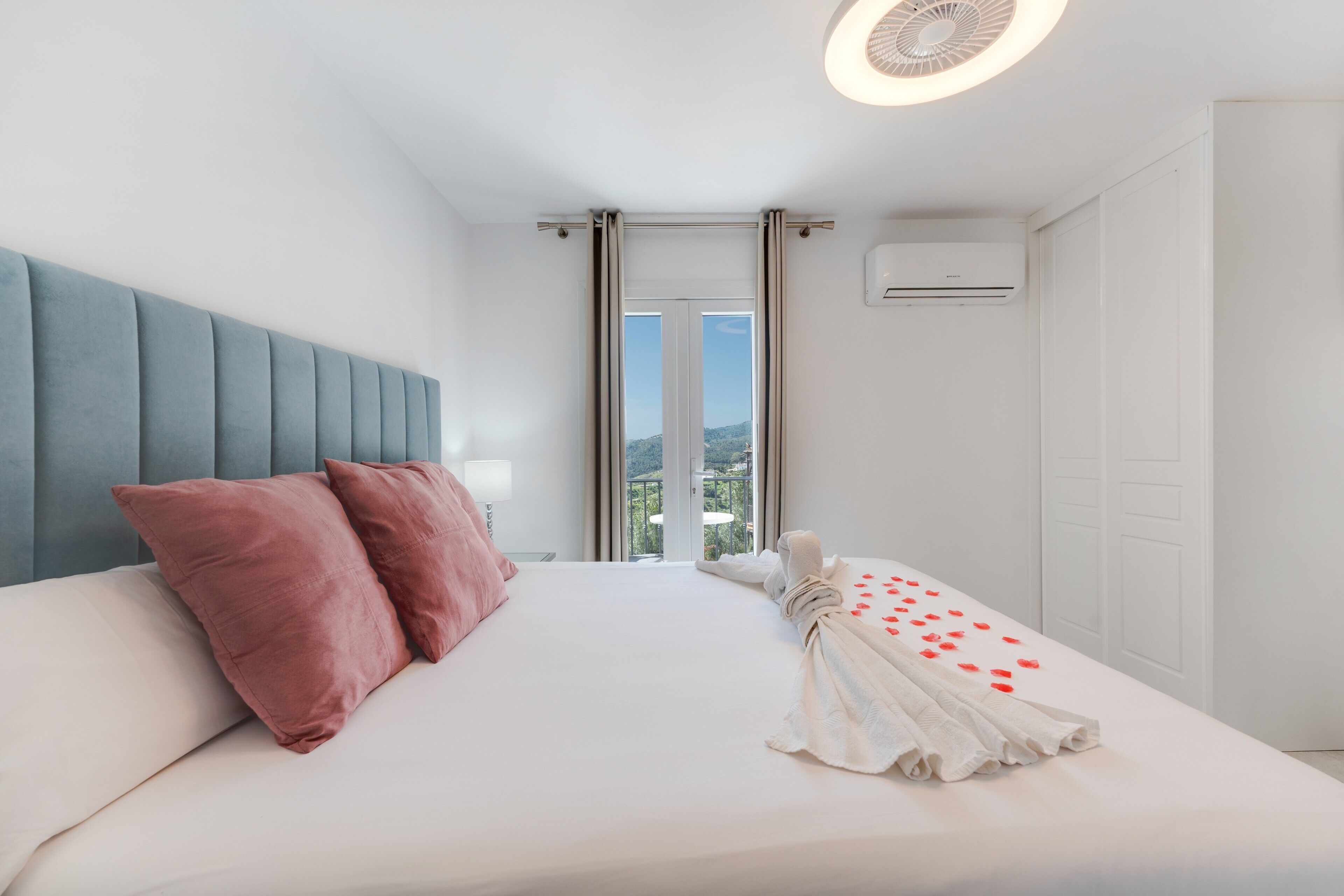 Habitación de hotel con cama, cabecero, unidad de aire acondicionado y vista a través de una puerta.