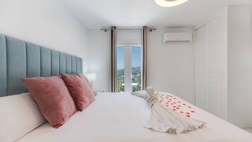 Habitación de hotel con cama, cabecero, unidad de aire acondicionado y vista a través de una puerta.