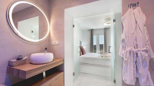 Ein modernes Badezimmer mit rundem Spiegel, Waschbecken in Weiß und einer Duschkabine aus Glas.